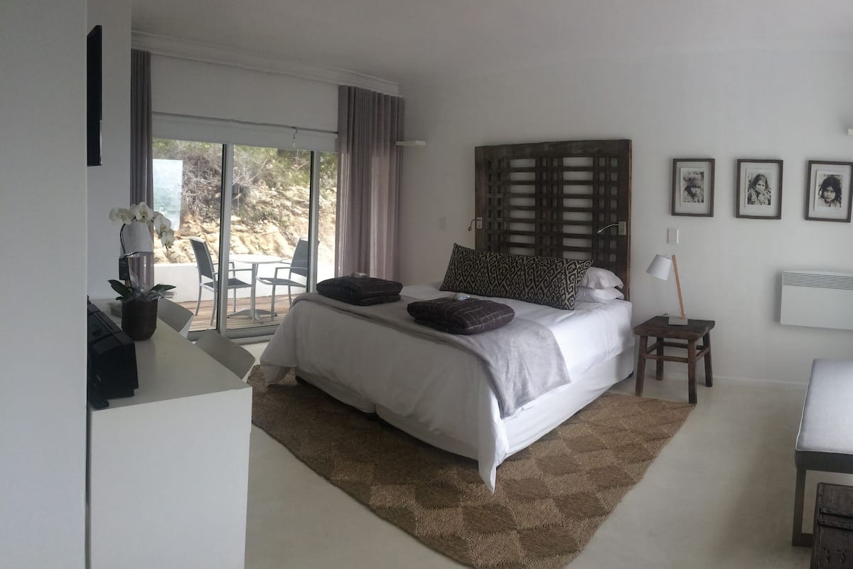 Une chambre avec un grand lit, une petite table, une chaise et une vue sur l’extérieur grâce à une porte coulissante.