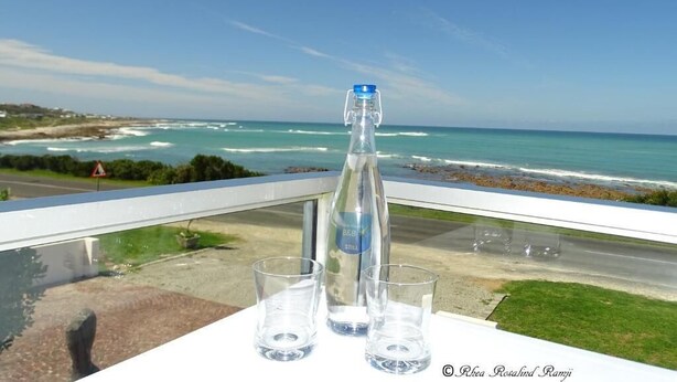 A balcony with a clear view of the ocean, a bottle of water, and two glasses.