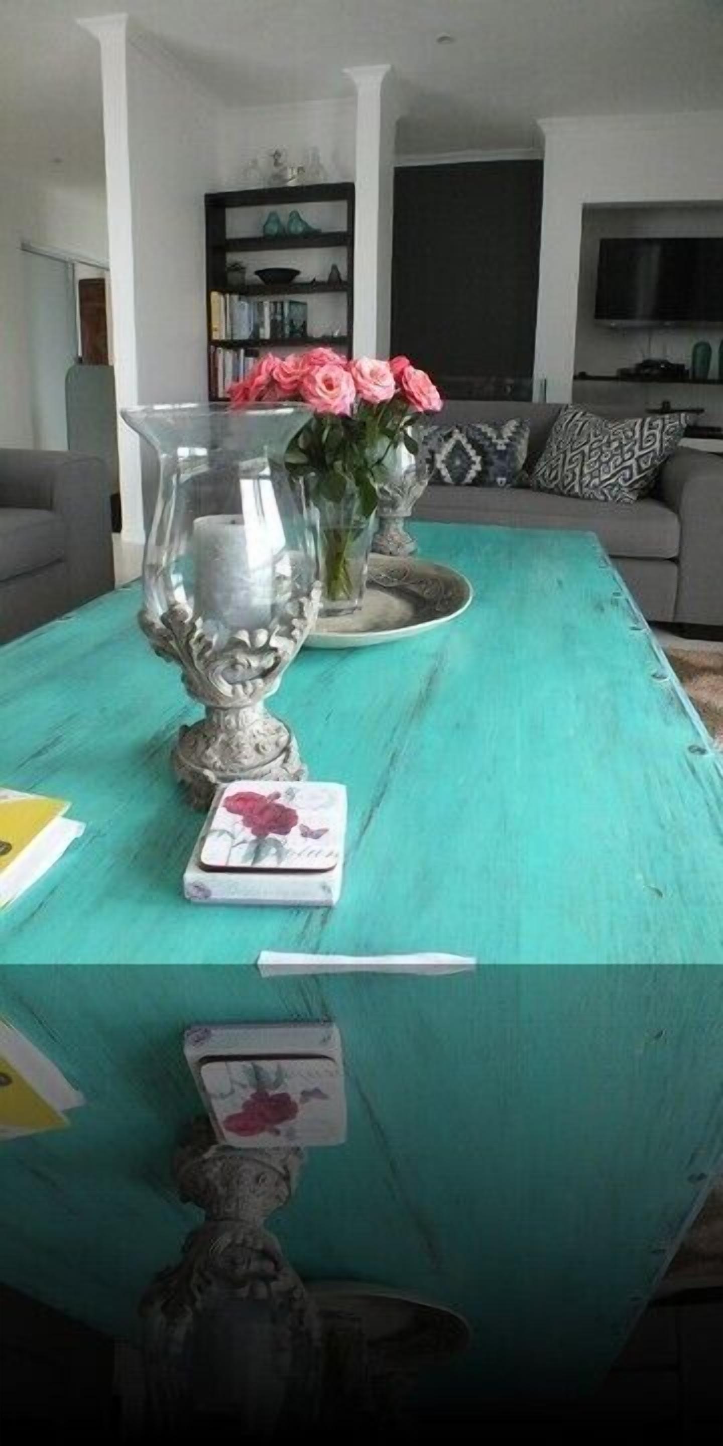 Una mesa color aguamarina con un jarrón decorativo, una tarjeta y una pequeña escultura.