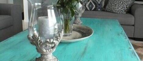 Una mesa color aguamarina con un jarrón decorativo, una tarjeta y una pequeña escultura.
