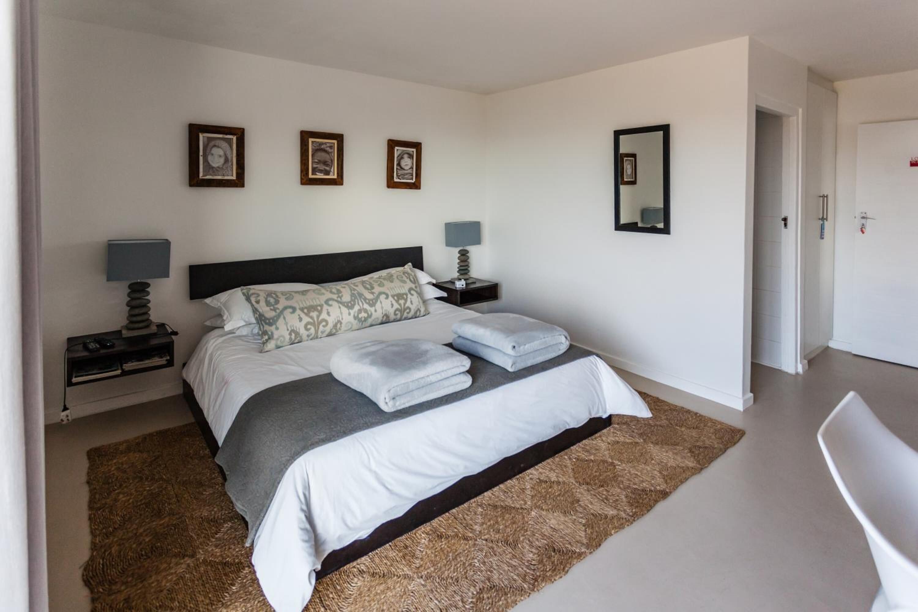 A bedroom with a bed, two bedside tables with lamps, a mirror, and framed pictures on the wall.