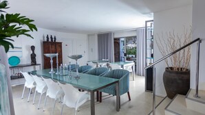 A modern dining area with a glass table and striped chairs, a staircase with a railing, and a view of the outdoors.