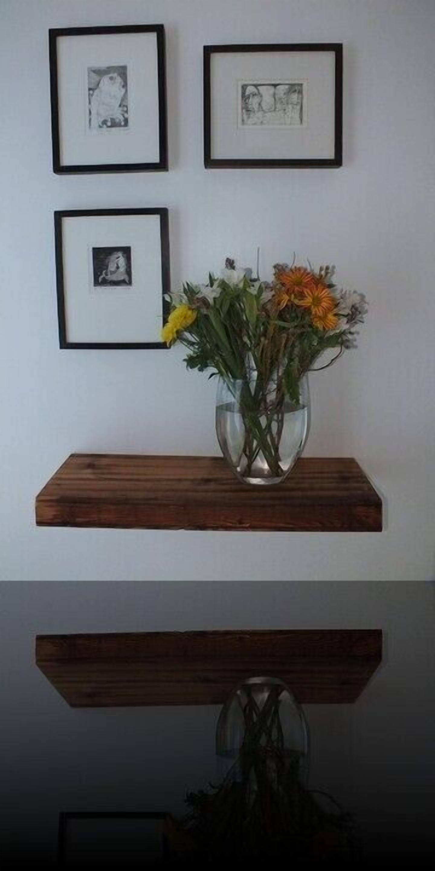 A wall with three framed pictures and a vase with flowers on a wooden shelf.