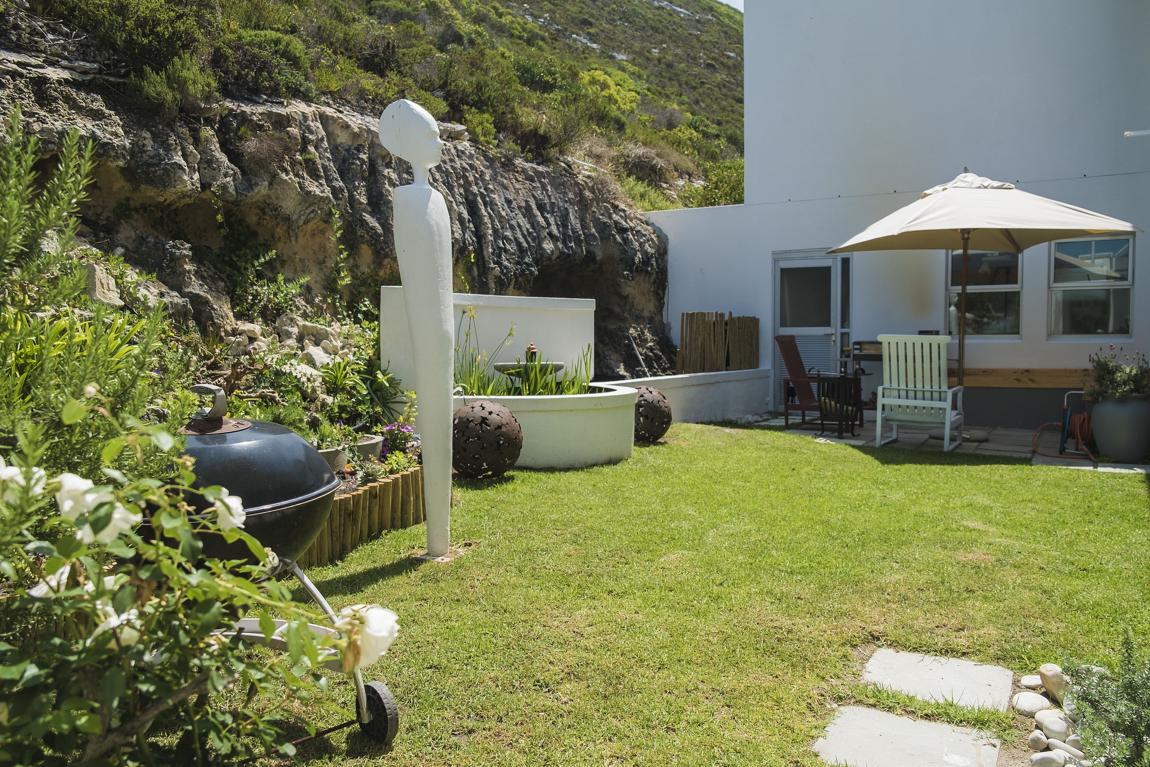 A backyard with a barbecue grill, outdoor seating, and a view of a rocky hillside.