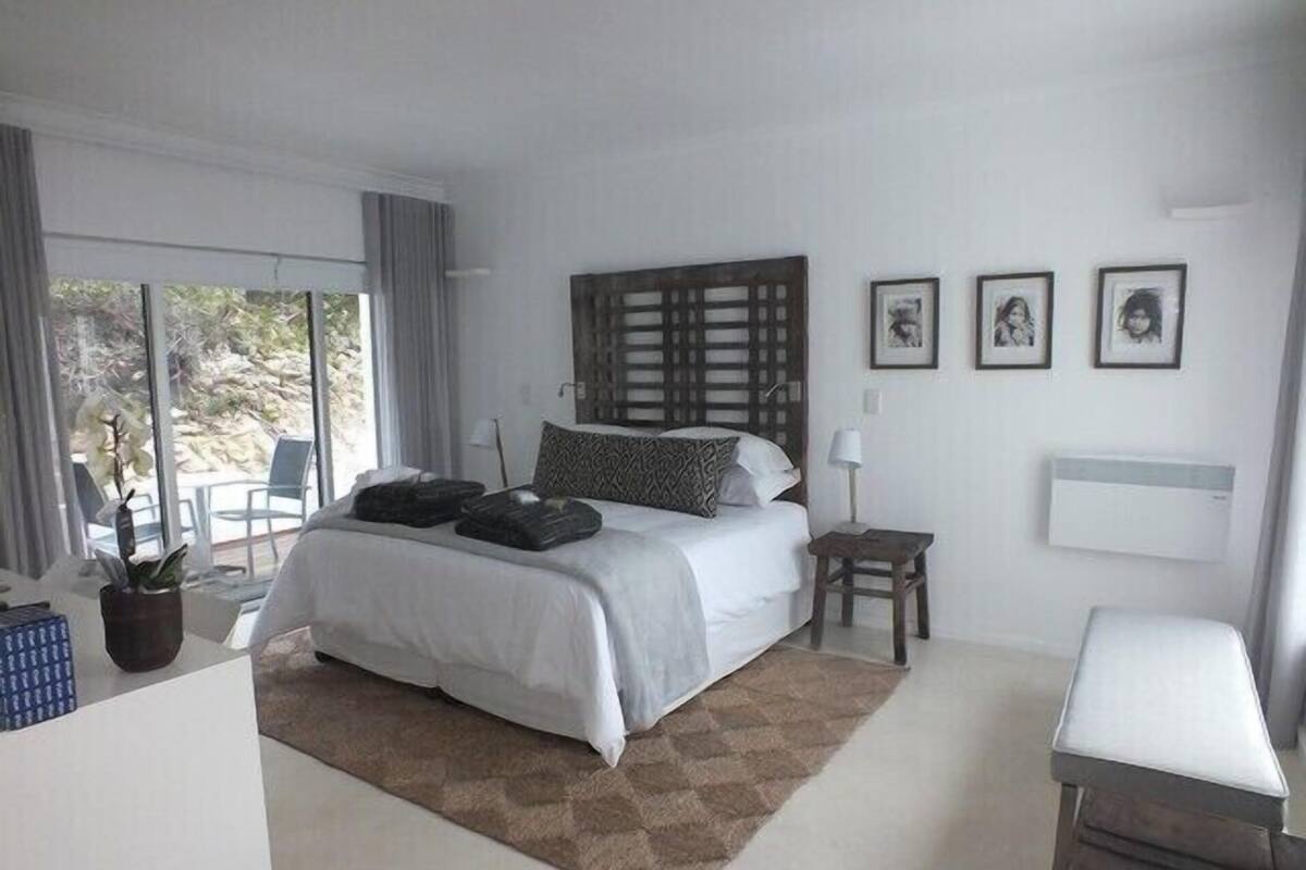Une chambre à coucher avec un lit, une petite table, une chaise, une plante en pot et une fenêtre avec des rideaux.