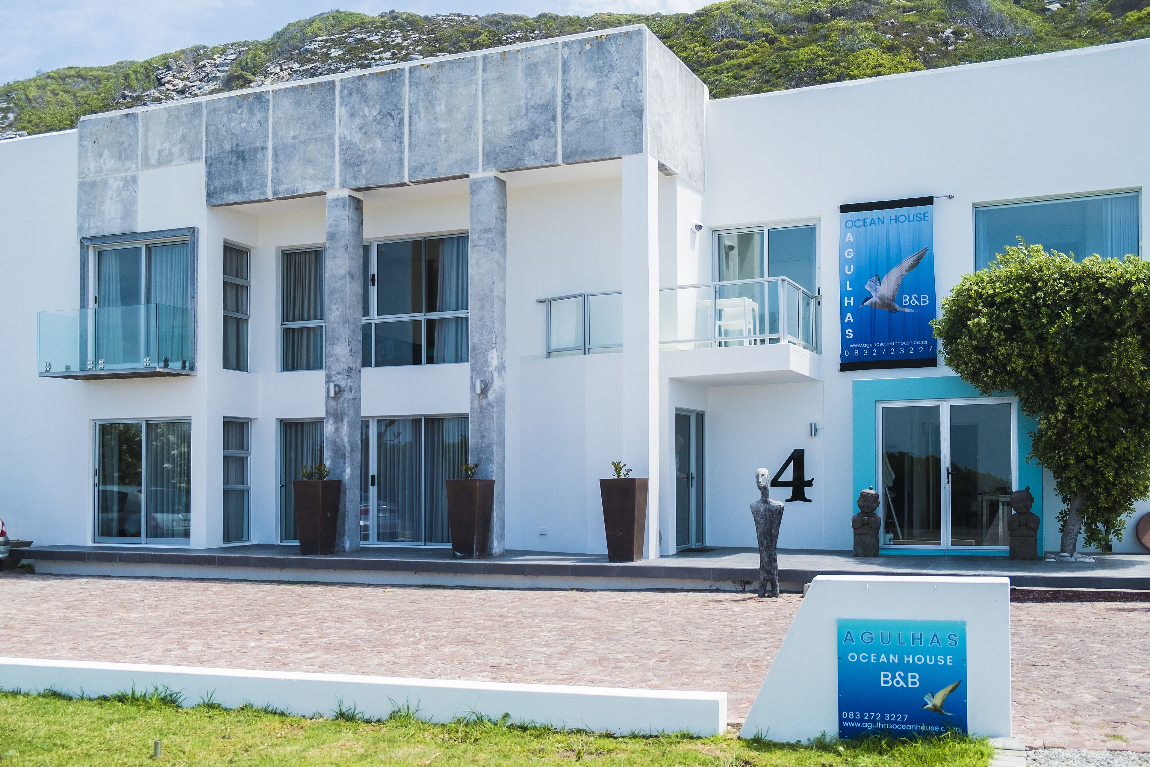 A modern building with large windows, a balcony, and a sign for 'AGULHAS OCEAN HOUSE B&B'.