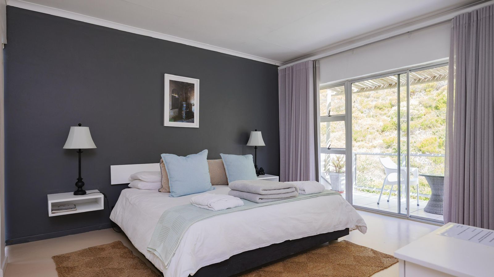 A bedroom with a bed, nightstands, a window with curtains, and a view of greenery outside.