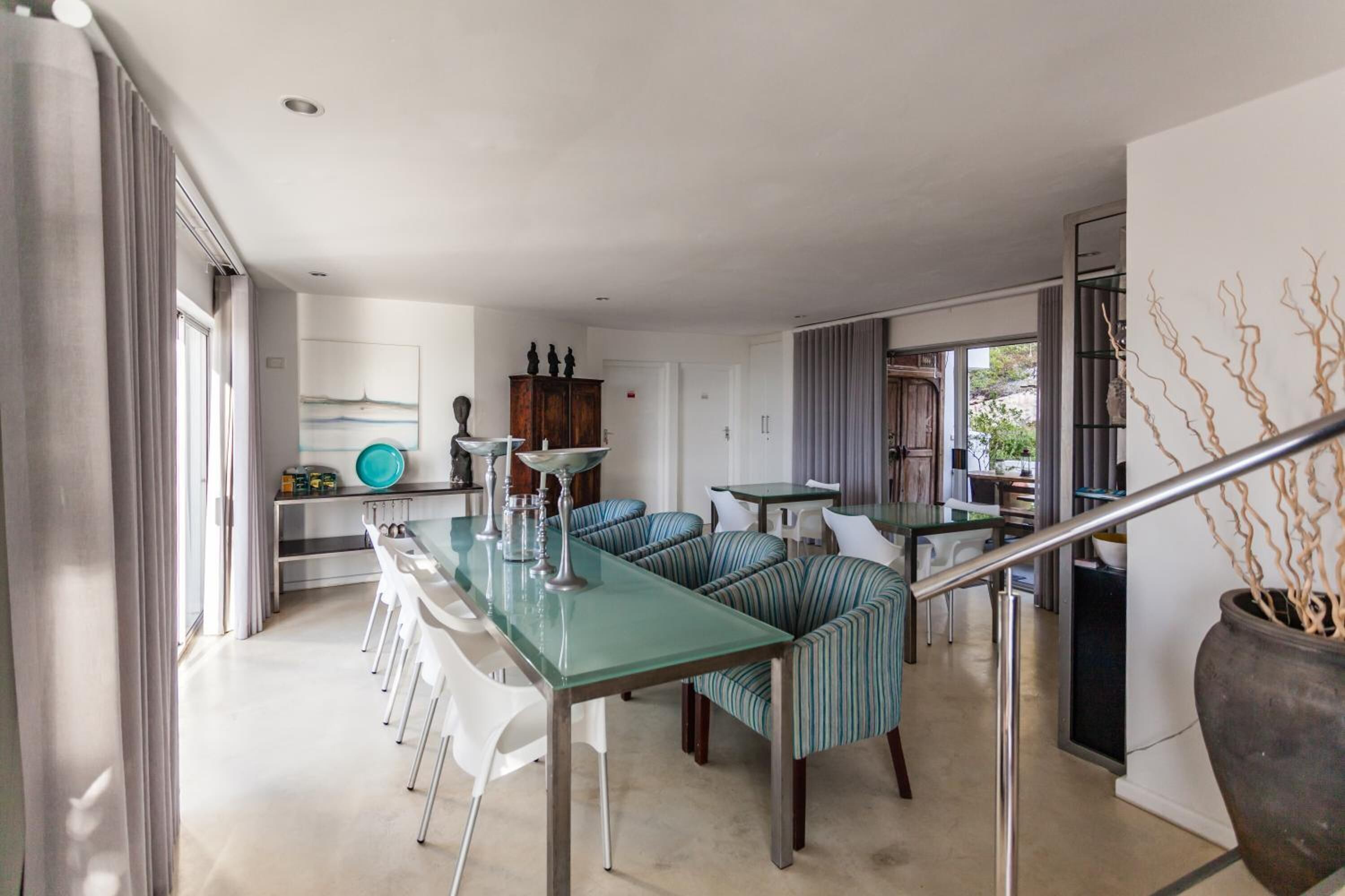 Una cocina moderna con una mesa de comedor de vidrio, asientos tapizados a rayas y una escalera con barandilla de metal.