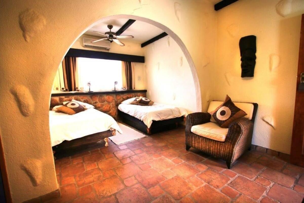 Una habitación acogedora con dos camas, una silla de mimbre y una pared de piedra.