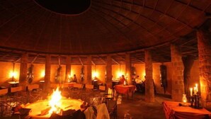 A circular room with a central fire, stone walls, and tables with red tablecloths. - Mount Etjo Safari Lodge (Omaruru)