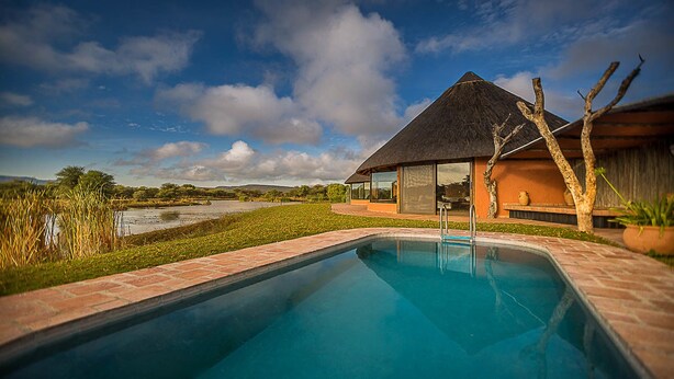 A swimming pool with a view of a house and landscape. - Mount Etjo Safari Lodge (Omaruru)