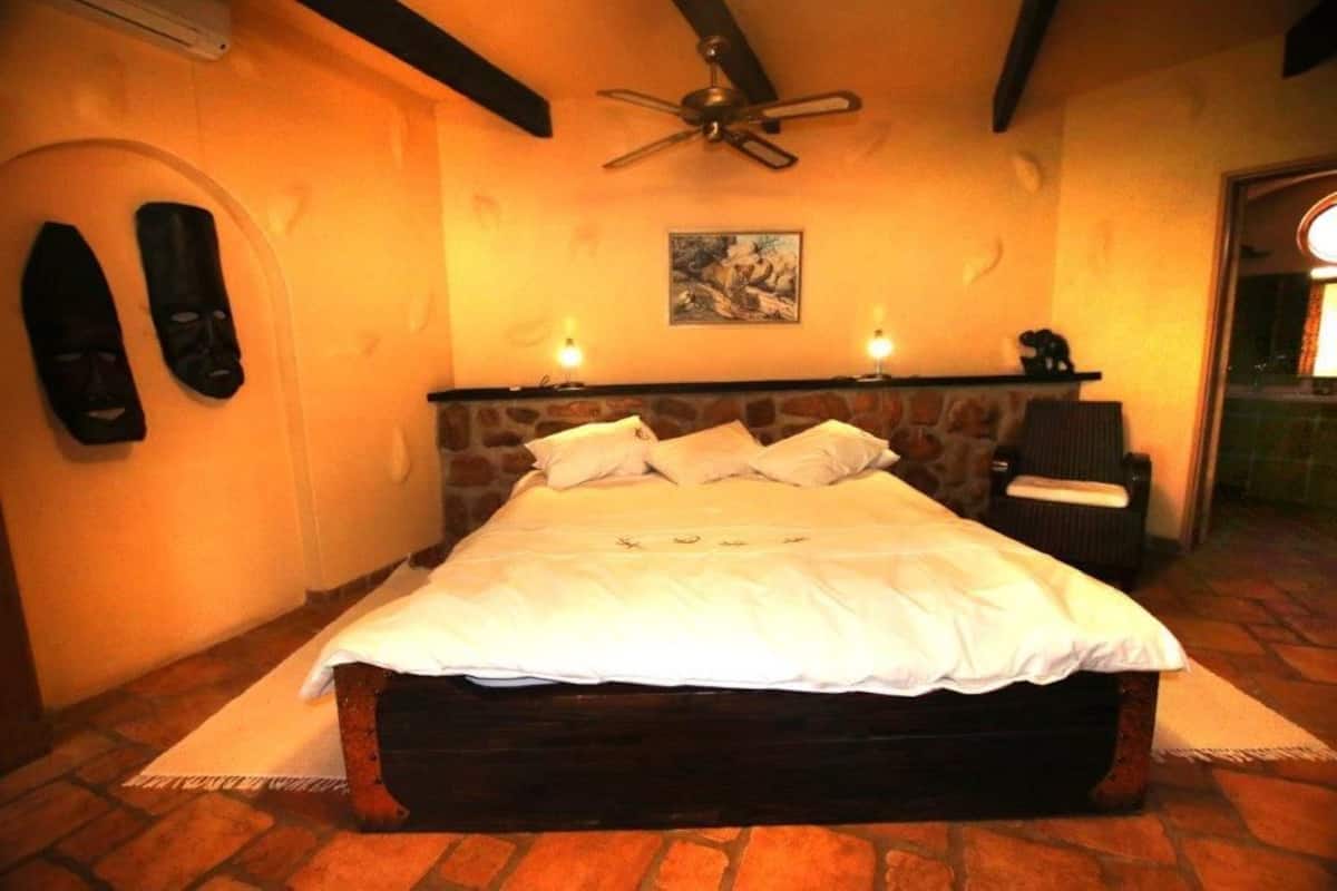 Un dormitorio con cabecera de piedra, cama con ropa blanca, dos lámparas de pared y un ventilador de techo.