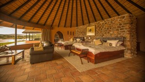 A spacious room with a high, thatched ceiling, a stone wall, and a large bed with two side tables. - Mount Etjo Safari Lodge (Omaruru)