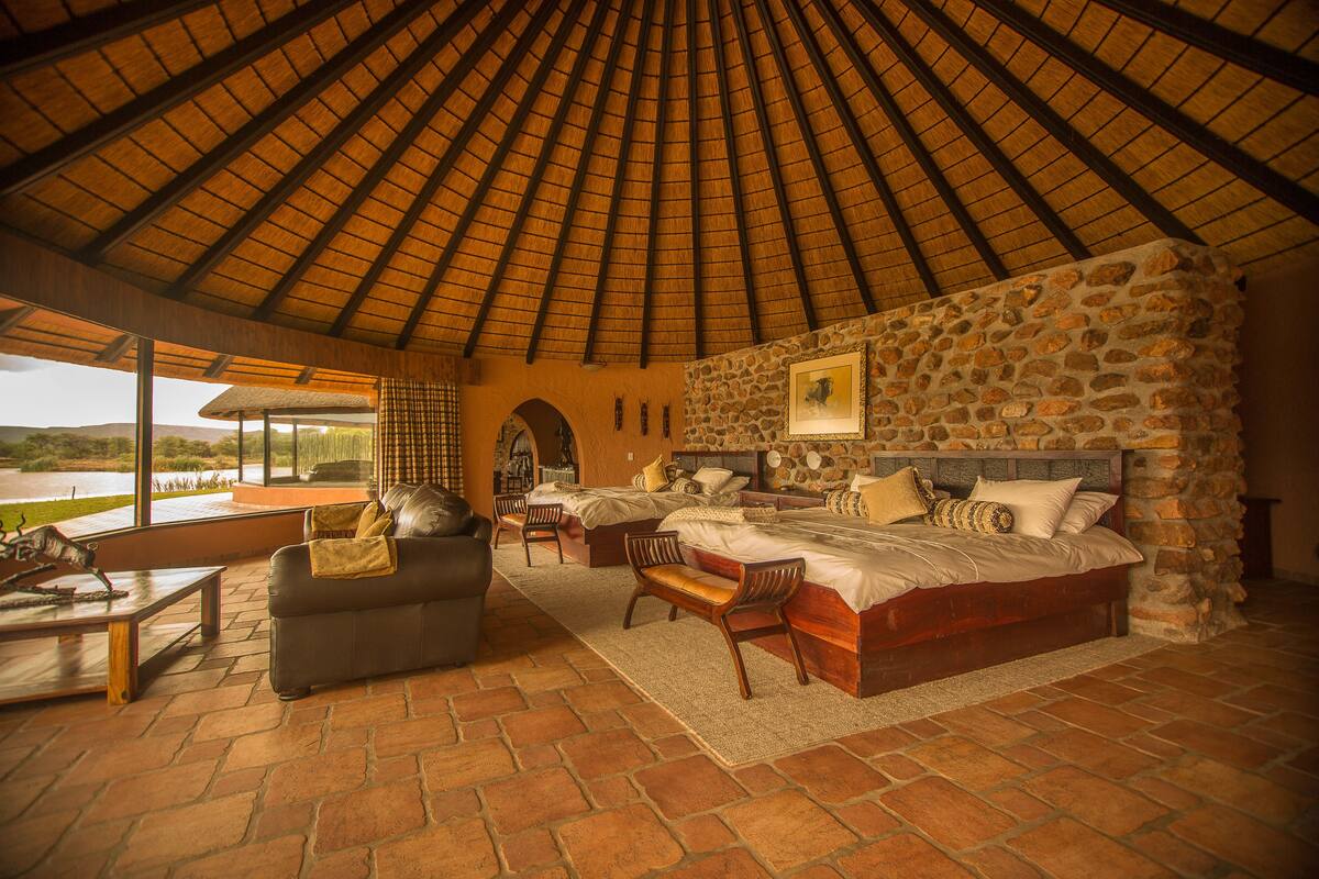 Una habitación amplia con un techo alto de paja, una pared de piedra y una cama grande con dos mesitas de noche.