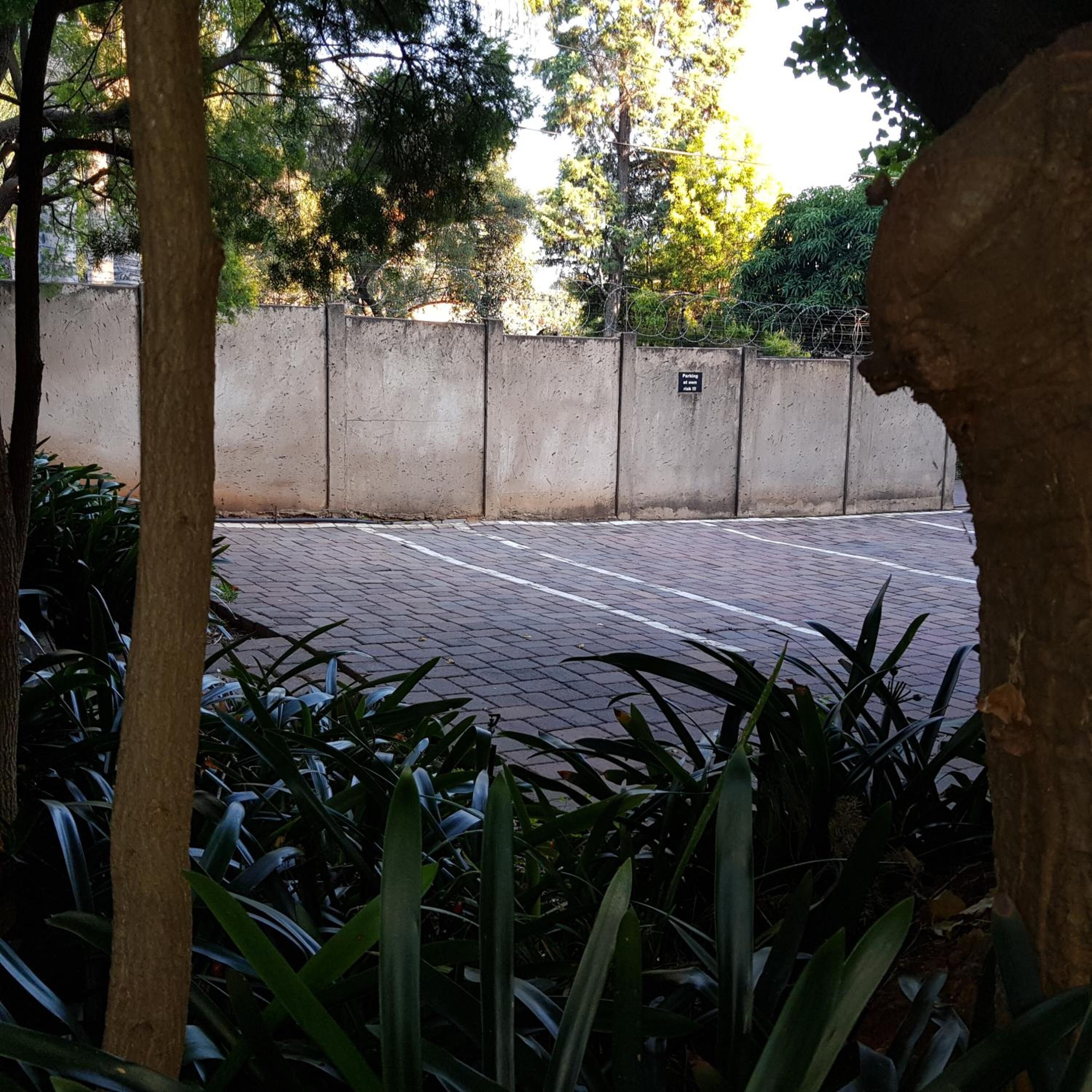 Un área de estacionamiento pavimentada con un muro de concreto y un cartel que indica restricciones de estacionamiento.