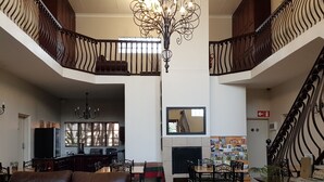 Ein geräumiger Wohnbereich mit hoher Decke, einer Chandelierleuchtre, einem Kamin und einer Treppe mit aufwendiger Geländerarbeiten.