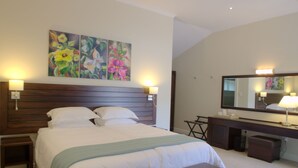 A hotel room with a large bed, a bedside table, a dresser, a mirror, and a painting on the wall.