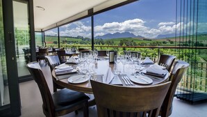 A dining area with a table set for six, overlooking a scenic landscape with mountains and fields.