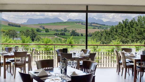 A restaurant with tables set for dining, overlooking a scenic landscape with mountains and fields.