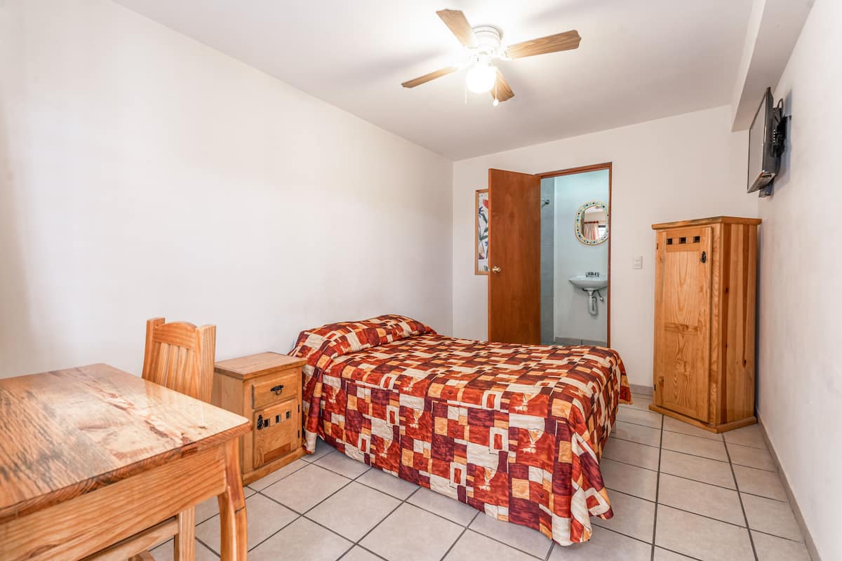 A bedroom with a wooden bed, a wooden nightstand, a wooden wardrobe, a wooden desk, and a ceiling fan.