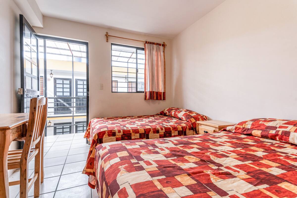 A room with two beds, a wooden chair, a table, and a window with curtains.