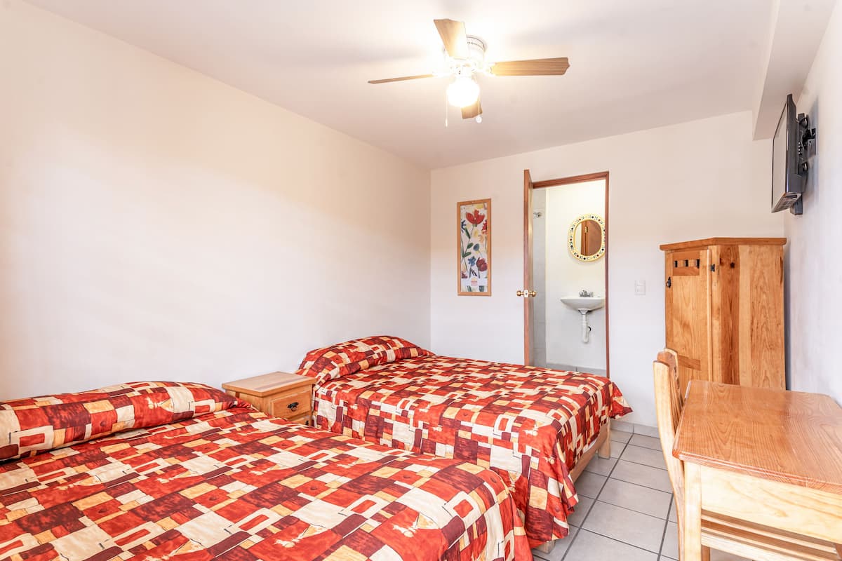 A bedroom with two beds, a wooden cabinet, a ceiling fan, and a wall-mounted TV.