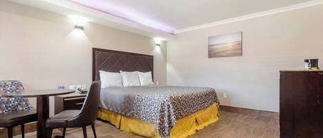 A bedroom with a bed, bedside table, chair, and a desk with a lamp.