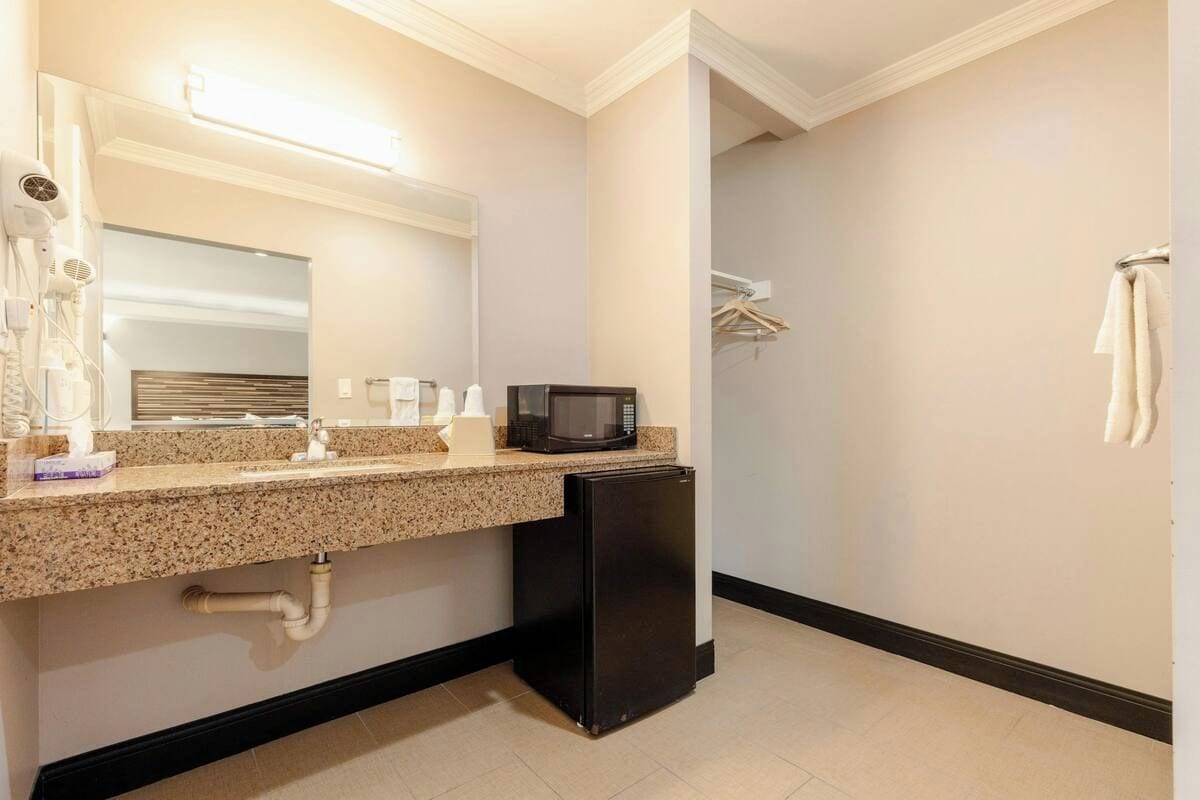 A bathroom with a sink, mirror, towel rack, and a microwave.