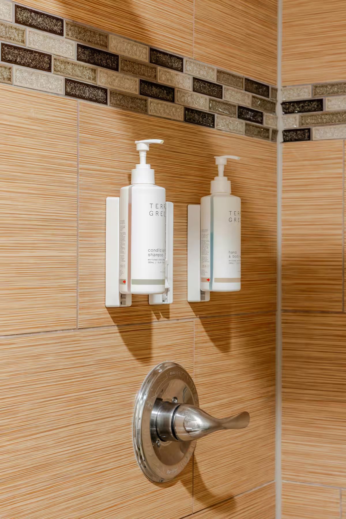 Un baño con pared de madera, puerta de ducha y dos botellas de champú y acondicionador.