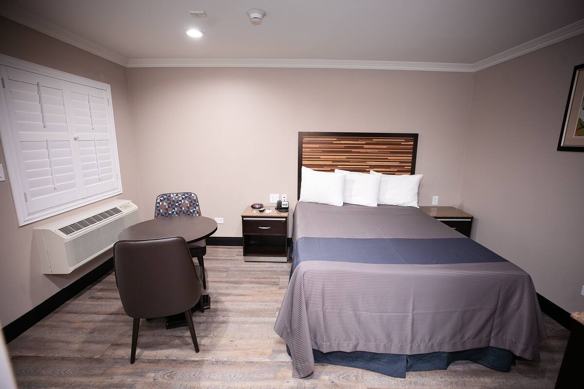 Une chambre d’hôtel équipée d’un lit, d’un bureau, d’une chaise, d’une table de chevet et d’un radiateur fixé au mur.