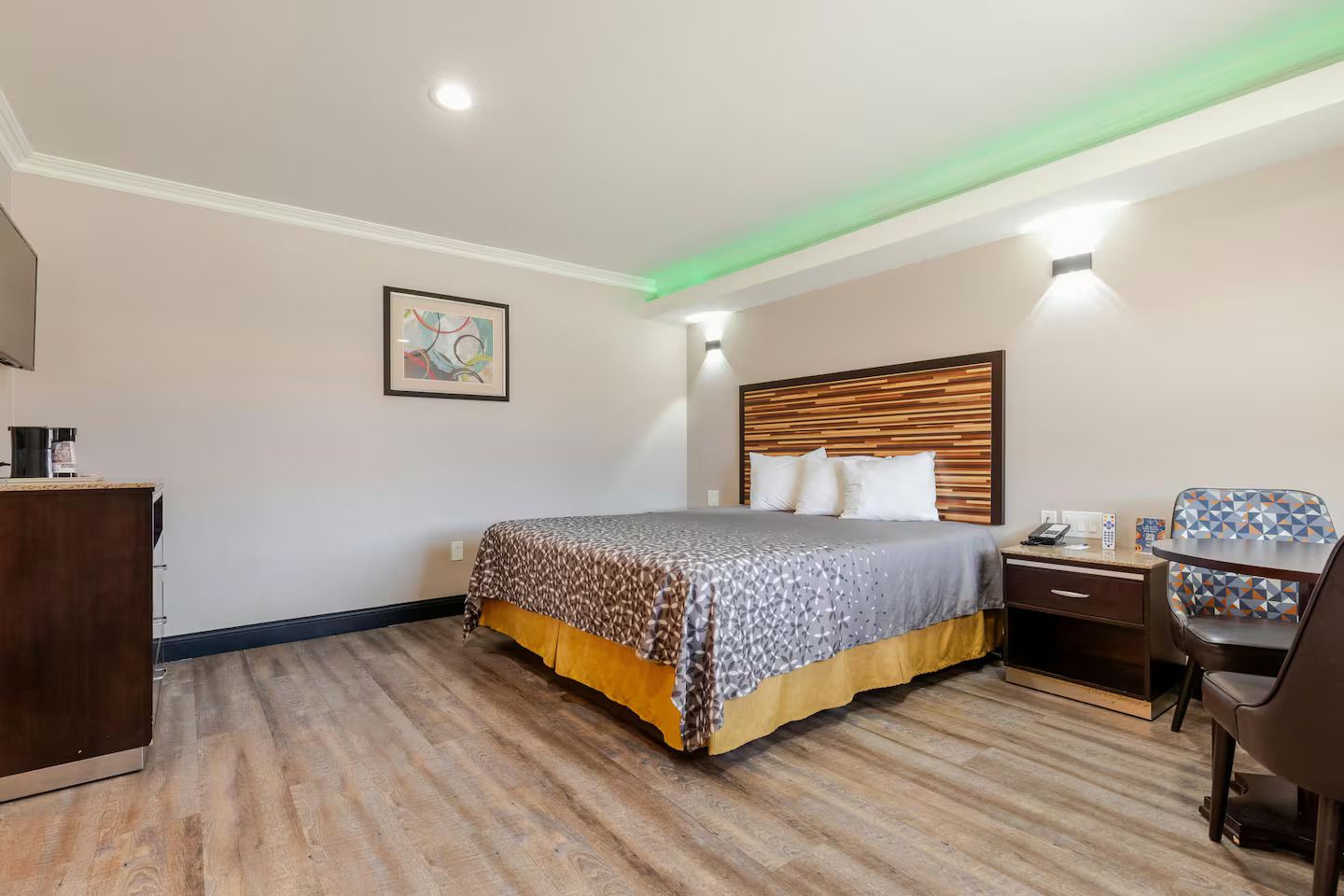 A hotel room with a bed, desk, chair, and a painting on the wall.