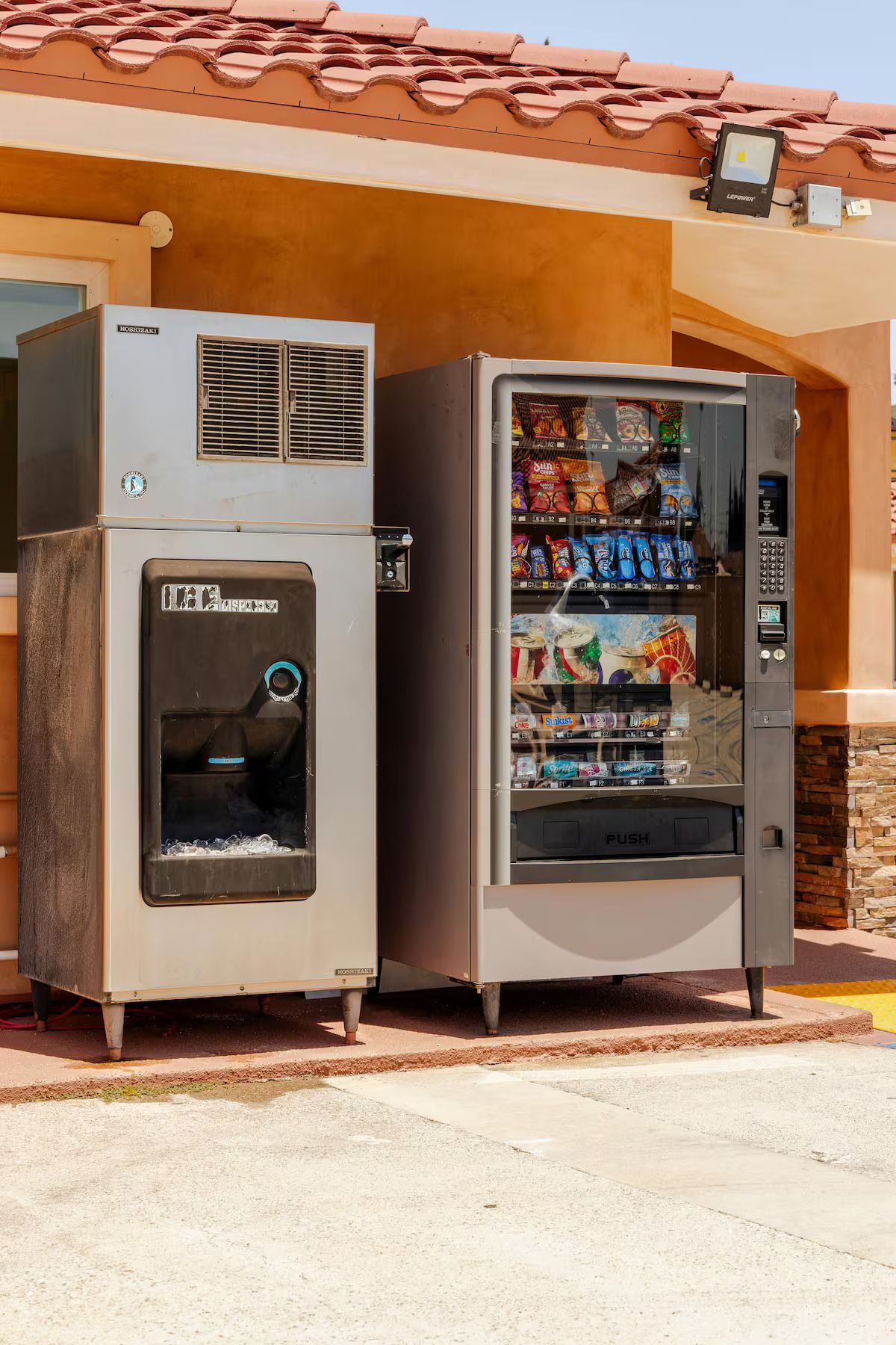 A vending machine and an air conditioning unit outside a building with a tiled roof.