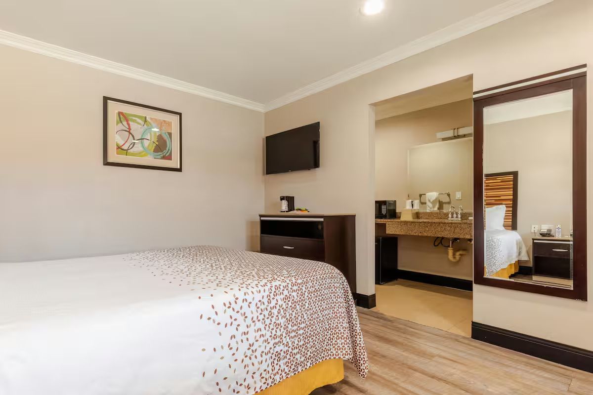 A hotel room with a bed, a desk, a television, and a bathroom visible through an open door.
