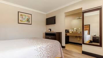A hotel room with a bed, a desk, a television, and a bathroom visible through an open door.