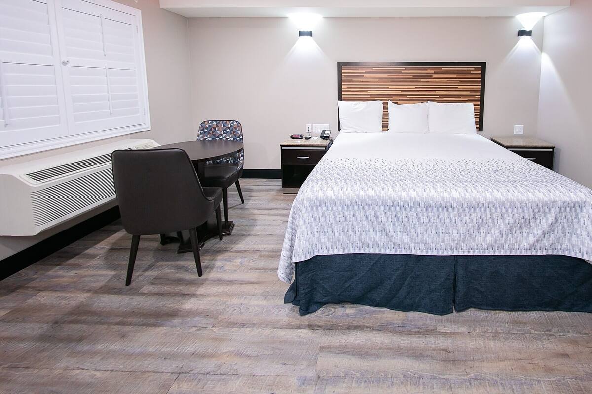 Une chambre d’hôtel comprenant un lit, un bureau avec une chaise, une table de chevet et un climatiseur fixé au mur.