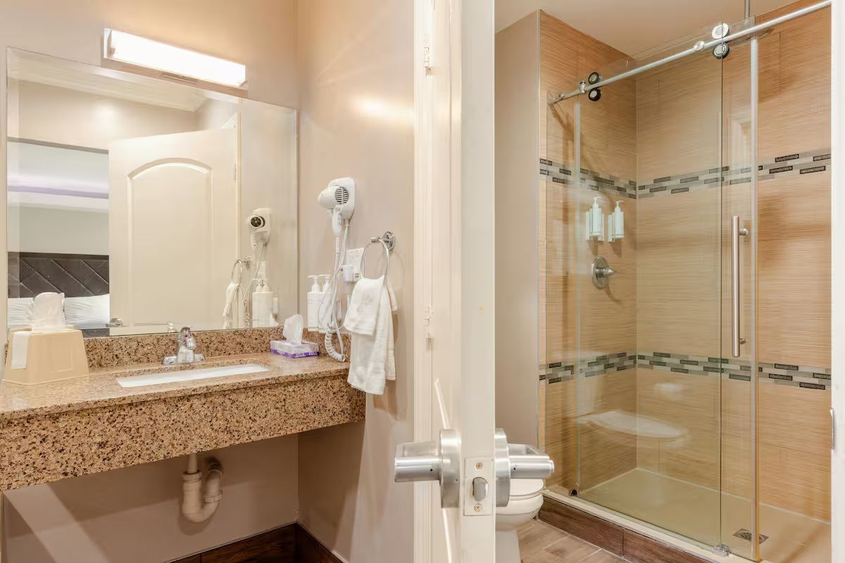 Une salle de bain dotée d’un comptoir en granit, d’un miroir, d’un sèche-cheveux et d’une douche à parois de verre.