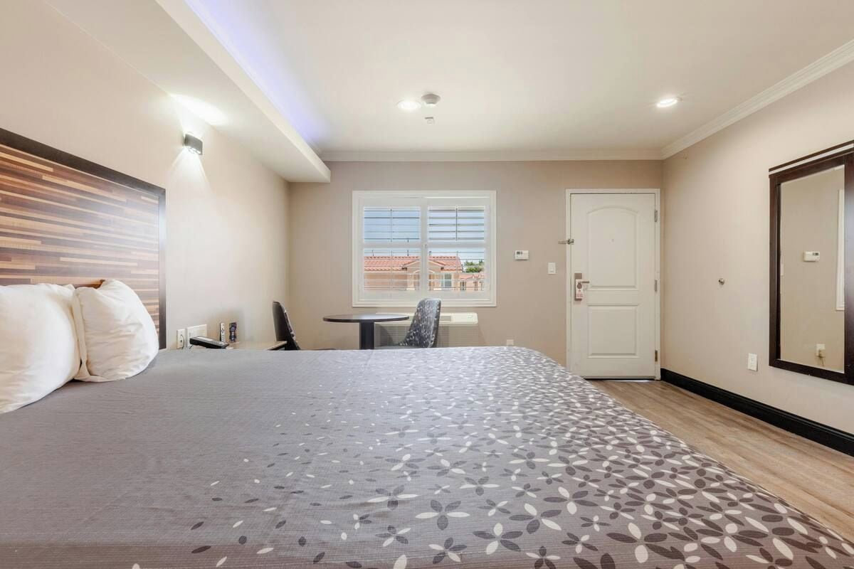 A hotel room with a bed, a desk, a chair, a window with blinds, and a door.
