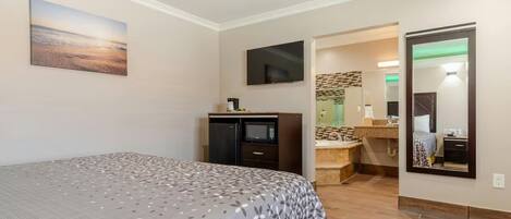 Ein Hotelzimmer mit Bett, Flachbildfernseher, Mikrowelle und einem durchgegangene Tür erkennbaren Badezimmer.
