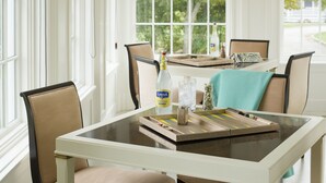Un coin repas avec une table dressée pour quatre personnes, entourée de chaises, avec une fenêtre donnant sur l’extérieur et une bouteille de limonade posée sur la table.