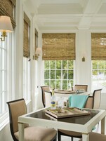 A dining area with a table set for four, surrounded by chairs, with a window view and a bottle of lemonade on the table.