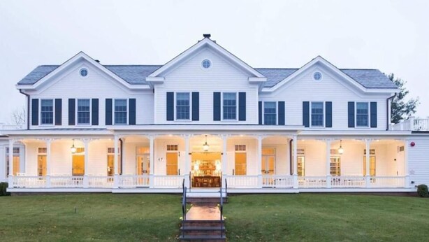 Un grand bâtiment blanc à deux étages, doté d’un porche avant couvert et de nombreuses fenêtres.