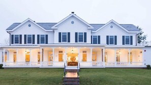 A large, two-story white building with a covered front porch and multiple windows. - The Quogue Club at Hallock House (Quogue)