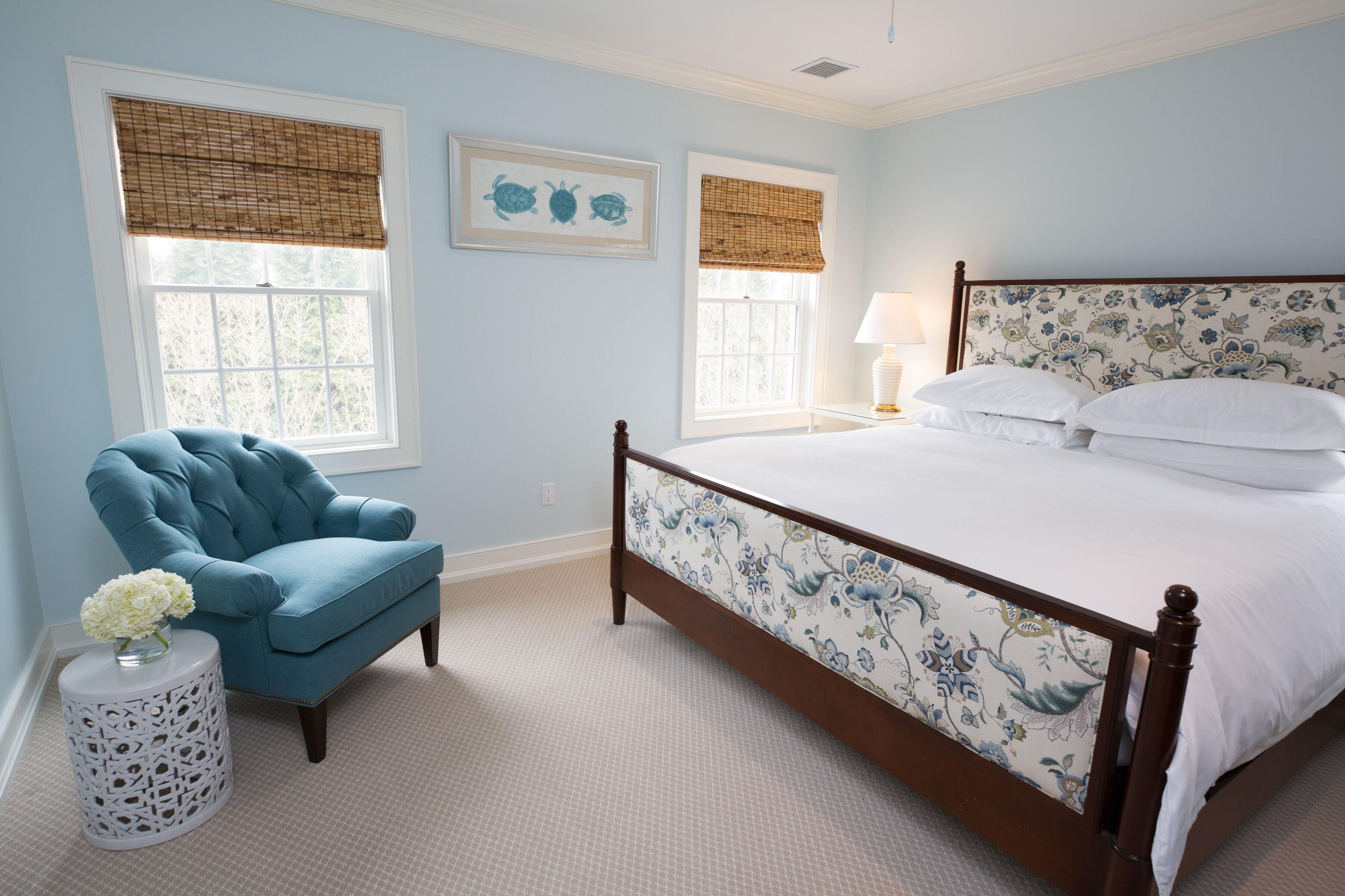 A bedroom with a bed, a chair, and two windows with blinds.