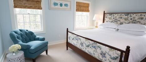 A bedroom with a bed, a chair, and two windows with blinds.