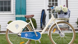 Un vélo avec un panier et une planche de surf appuyée contre une maison.