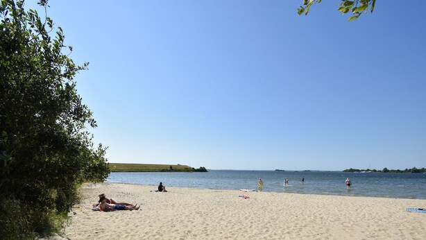 A sandy beach with people sunbathing and swimming.