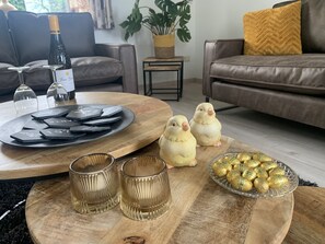A cozy living room with a wooden coffee table, two decorative bird figurines, a tray with playing cards, a bottle of wine, and a bowl of chocolates. - Cosy holiday home with large garden (Zonnemaire)