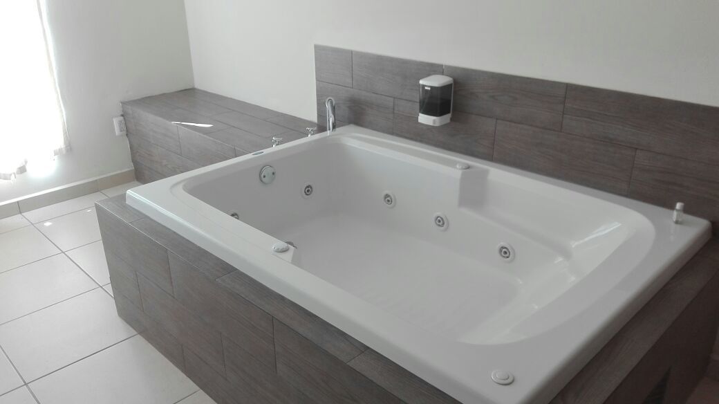 Un bagno moderno con una vasca da bagno ampia, una panca integrata e un erogatore di sapone a parete.