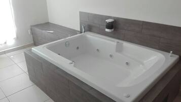 Un bagno moderno con una vasca da bagno ampia, una panca integrata e un erogatore di sapone a parete.