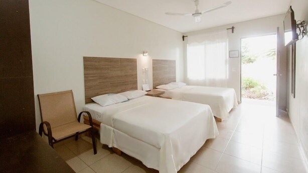 A hotel room with two beds, a chair, a ceiling fan, and a window with curtains. - Hotel Guivá San Pablo (Oaxaca)